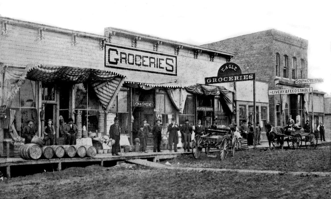 barrel, Animals, livery, horse, Lemberger, LeAnn, Cities and Towns, history of Iowa, Main Streets & Town Squares, Iowa History, wagon, Portraits - Group, Iowa, Businesses and Factories, store, cart, Ottumwa, IA, feed stable, dirt road, grocery store, awning