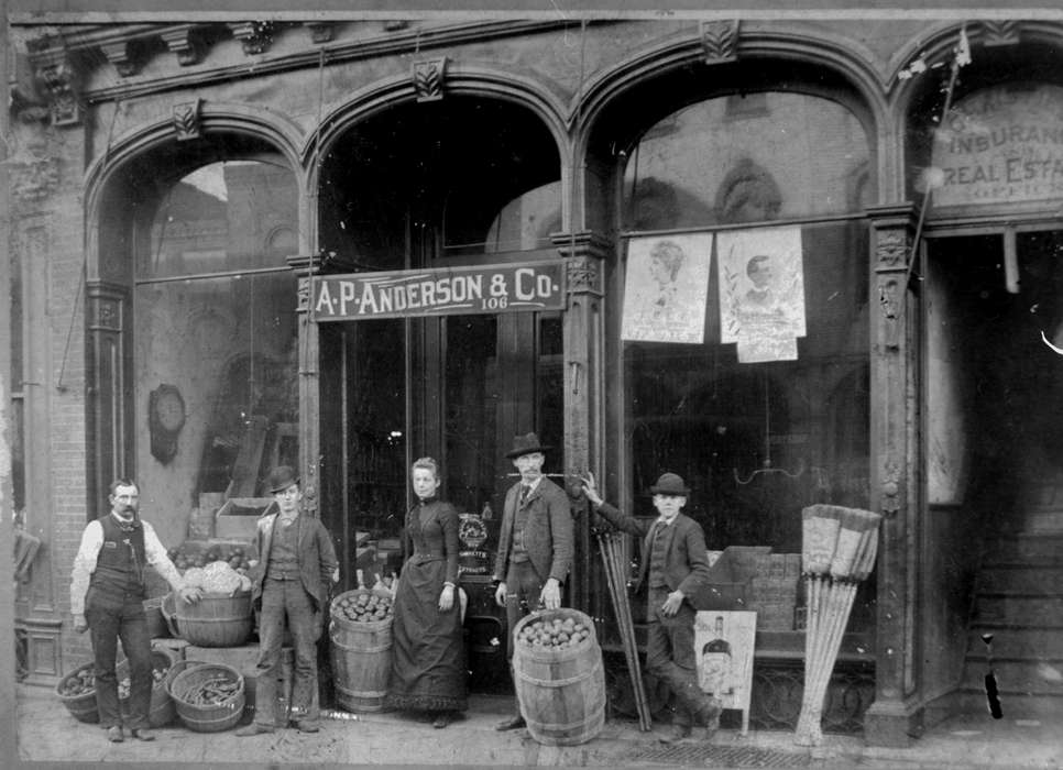 Food and Meals, barrel, storefront, business owner, broom, Lemberger, LeAnn, Cities and Towns, fruit, history of Iowa, apple, Main Streets & Town Squares, Iowa History, Portraits - Group, Iowa, suit, Businesses and Factories, window display, sign, Ottumwa, IA, grocery store