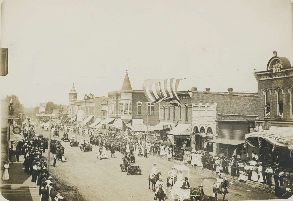 Aerial Shots, clock, Waverly Public Library, history of Iowa, Businesses and Factories, umbrella, brick building, automobile, bank, parade, Cities and Towns, american flag, Motorized Vehicles, dirt street, Iowa History, Entertainment, Iowa, correct date needed, Animals, car, horse, crowd, clock tower, carriage, Main Streets & Town Squares