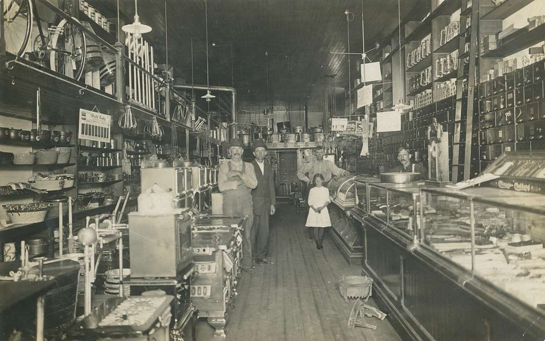 Portraits - Group, light, girl, hardware store, Businesses and Factories, stove, man, lamp, Waverly Public Library, building interior, history of Iowa, Iowa History, bowler hat, bicycle, clock, overalls, suspenders, display case, Iowa, moustache, barrel, correct date needed, Children, suit, Labor and Occupations